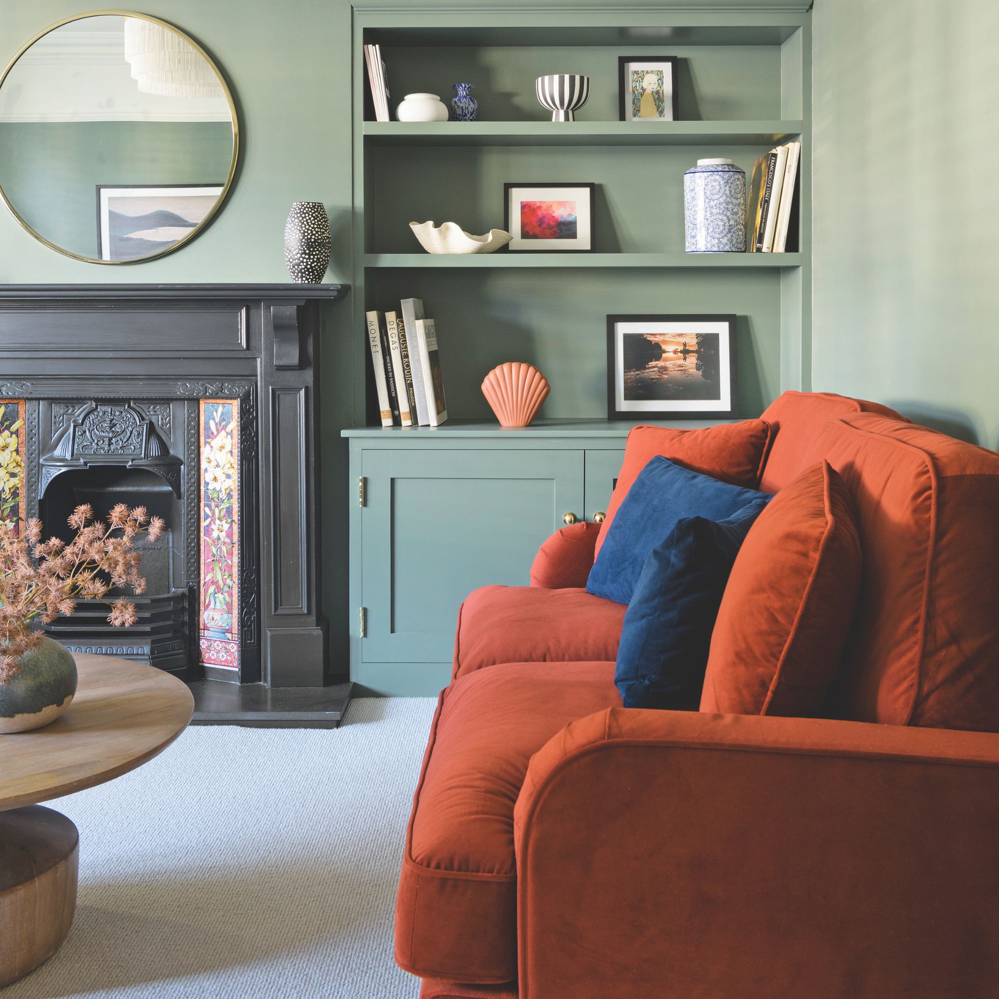 Green living room with an orange sofa, a period fireplace and a mirror above it