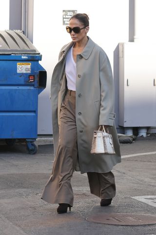 Jennifer Lopez in a khaki trench coat, white tee shirt, and trousers