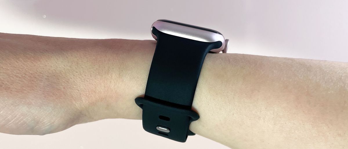 A black silicone Apple Watch-compatible strap is worn on a woman&#039;s wrist, with the side of the watch visible at the top of her wrist.