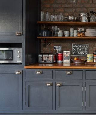 navy blue kitchen with exposed brick wall, shelving and microwave