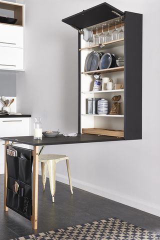 A white kitchen with a black storage unit attached to a wall with a drop down table leaf