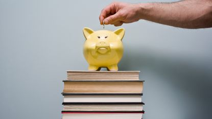 Man drops coin into a piggy bank balanced on top of a stack of books