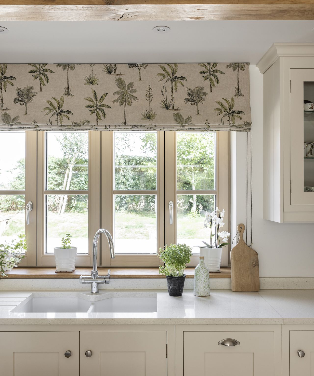 A quaint window in kitchen dressed with fabric blinds and a neutral tone kitchen design