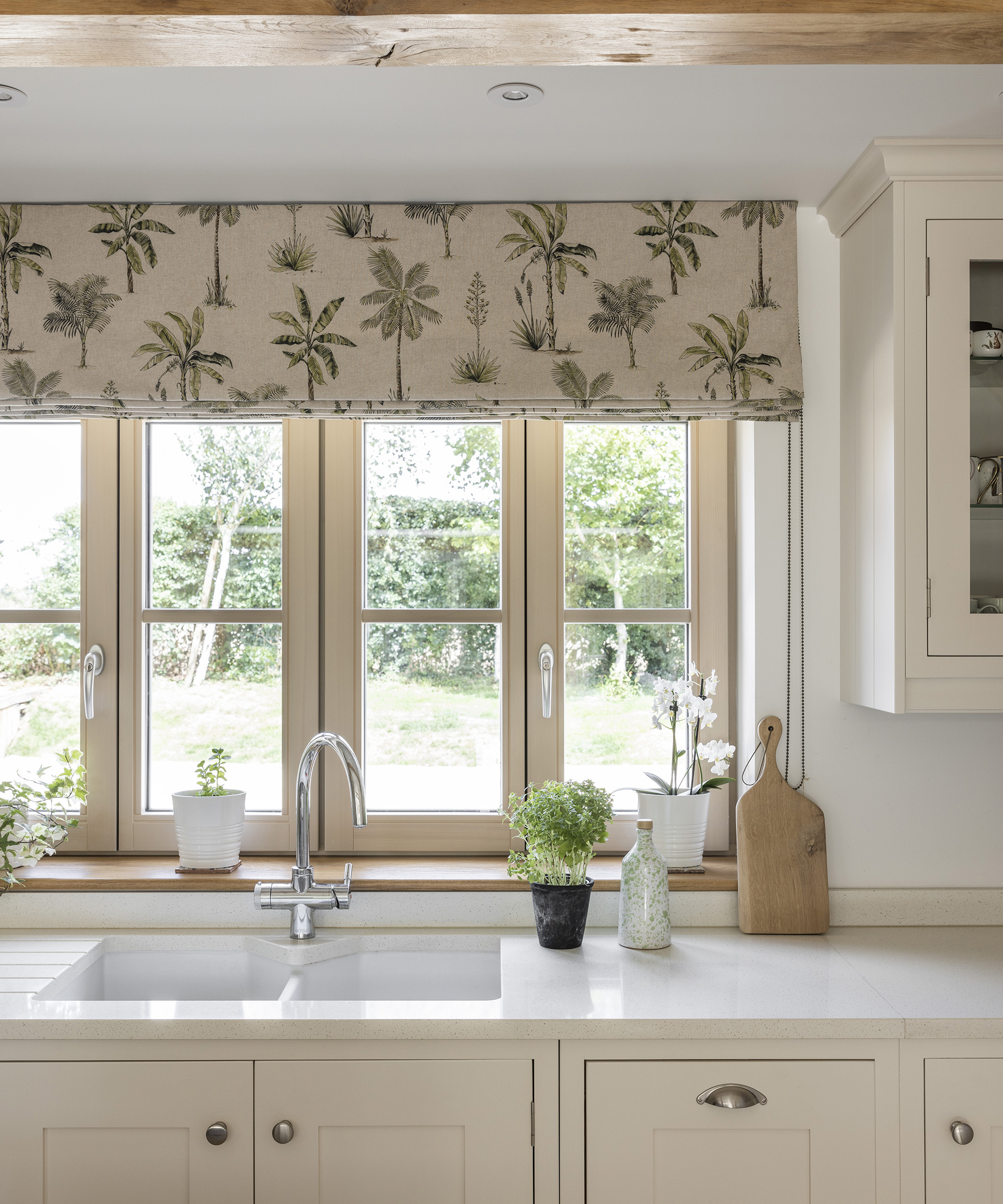 A quaint window in kitchen dressed with fabric blinds and a neutral tone kitchen design