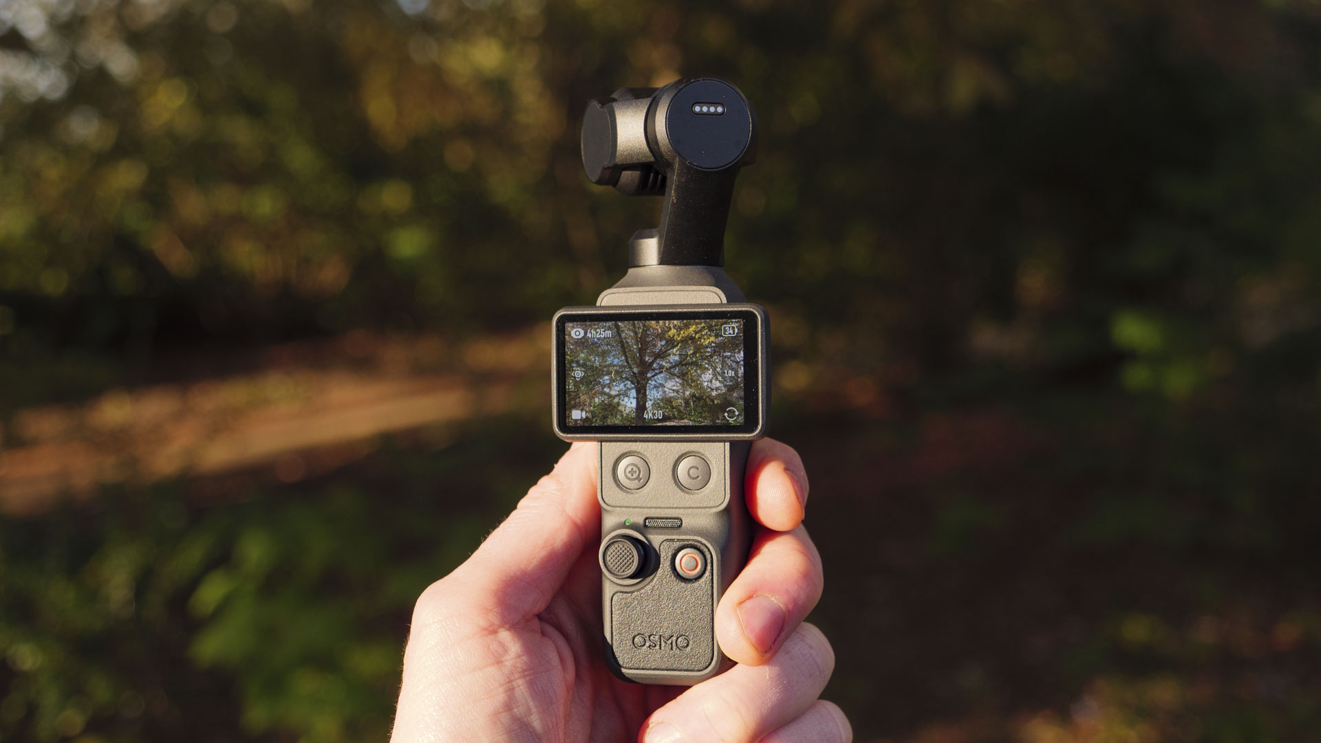DJI Osmo Pocket 4 vlogging camera in the hand with natural background at golden hour