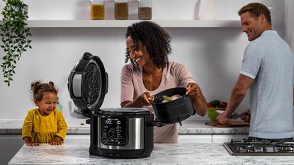 family in the kitchen using the Ninja Foodi Max 9-in-1 Multi cooker 7.5L and adding fry basket