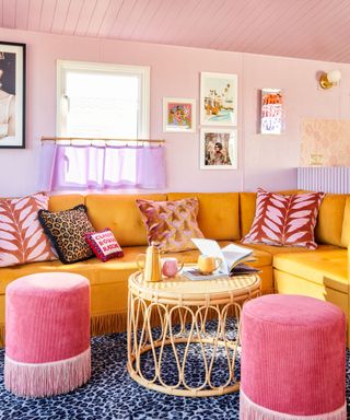 A pink living room with a yellow couch, rattan table, and pink stools