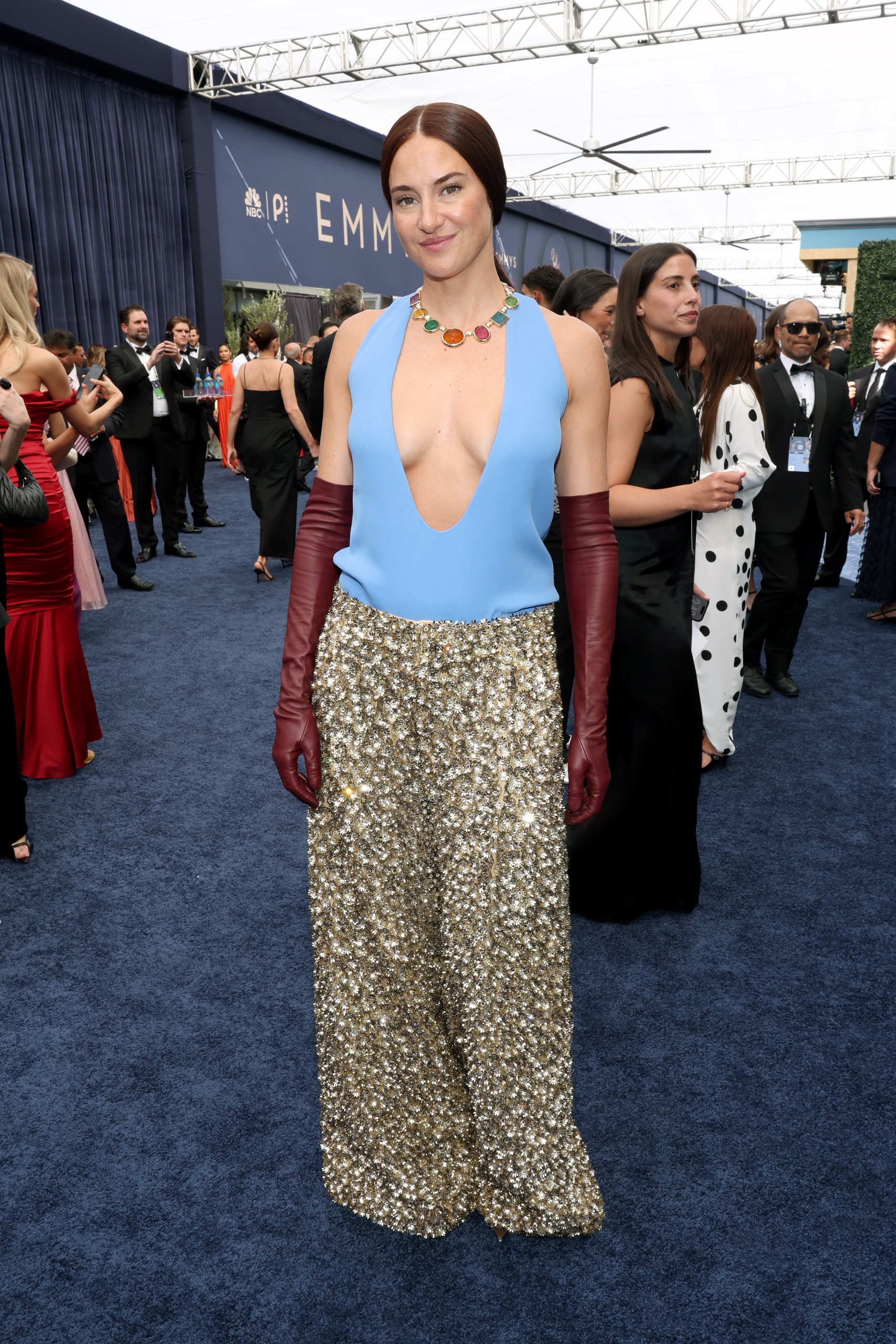 a white woman with a low brown ponytail in a blue top and sparkly pants with red gloves