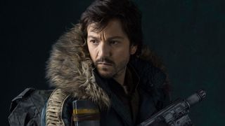 Diego Luna's Cassian Andor looks behind himself, with gun primed for action, in Star Wars: Rogue One