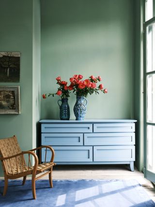 Powder blue drawers with blue vases and red flowers against a pale green wall