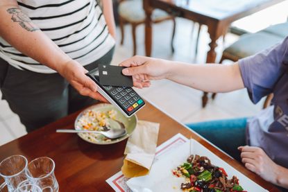 A person taps a credit card on a machine to pay a bill at a restaurant in the daytime.