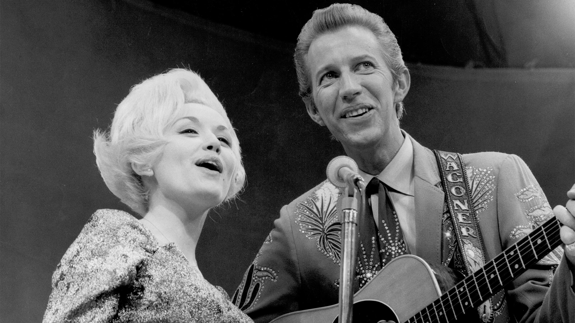 Country singer Dolly Parton and her collaborator Porter Wagoner perform onstage in circa 1967. Mr. Wagoner is wearing a Nudie Suit designed by Nudie Cohn of Nudie's Rodeo Tailors.