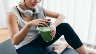A woman drinking a green smoothie, presumably with spirulina powder blended in.