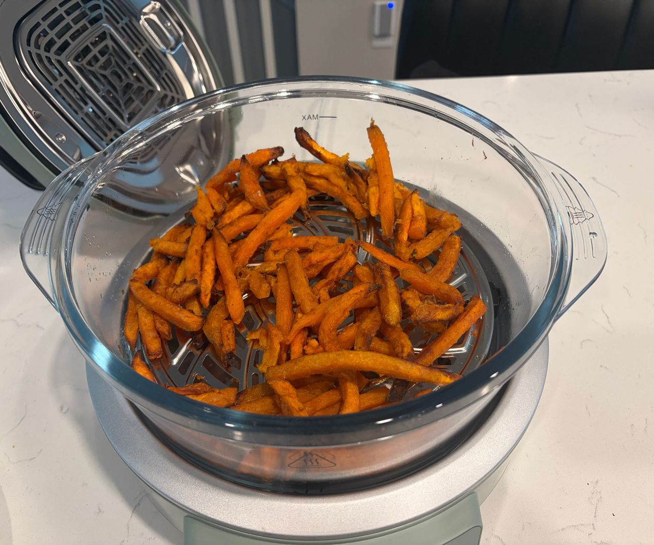 Sweet potato fries inside the glass basin of an air fryer on a white counter.