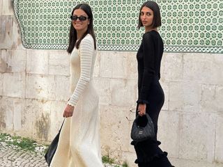 French influencer Salome Mory and her mother walk on a sidewalk in Lisbon, Portugal, wearing black and beige knitted long-sleeved maxi dresses with black pockets and black Mary Jane ballet flats