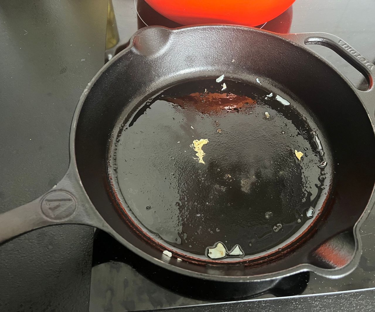 A greasy black cast iron pan with some small remnants of egg on it.