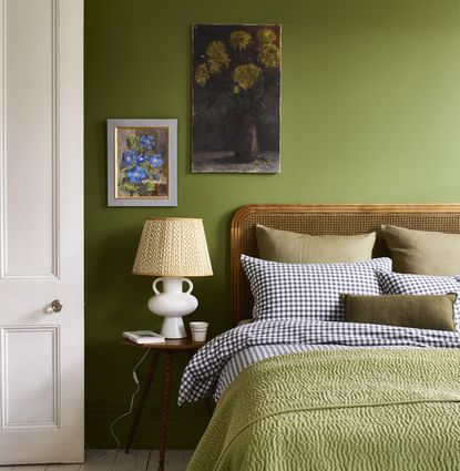 A green bedroom with bedside lamp and wooden and cane bed headboard
