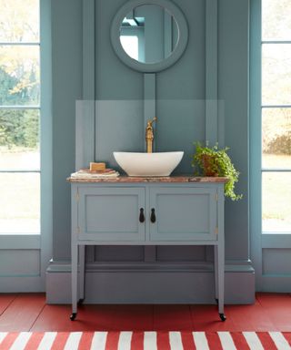 color drenched light blue bathroom with a red floor and red and white stripe rug