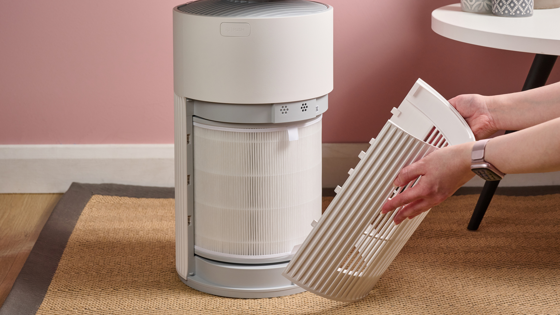 A woman is removing the side panel of the air purifier.