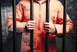 orange-jumpsuit-wearing prisoner grips bars of cell