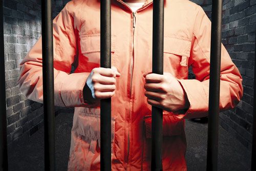 orange-jumpsuit-wearing prisoner grips bars of cell