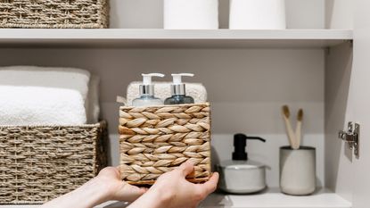 Person placing wicker basket filled with bathroom products into a cabinet