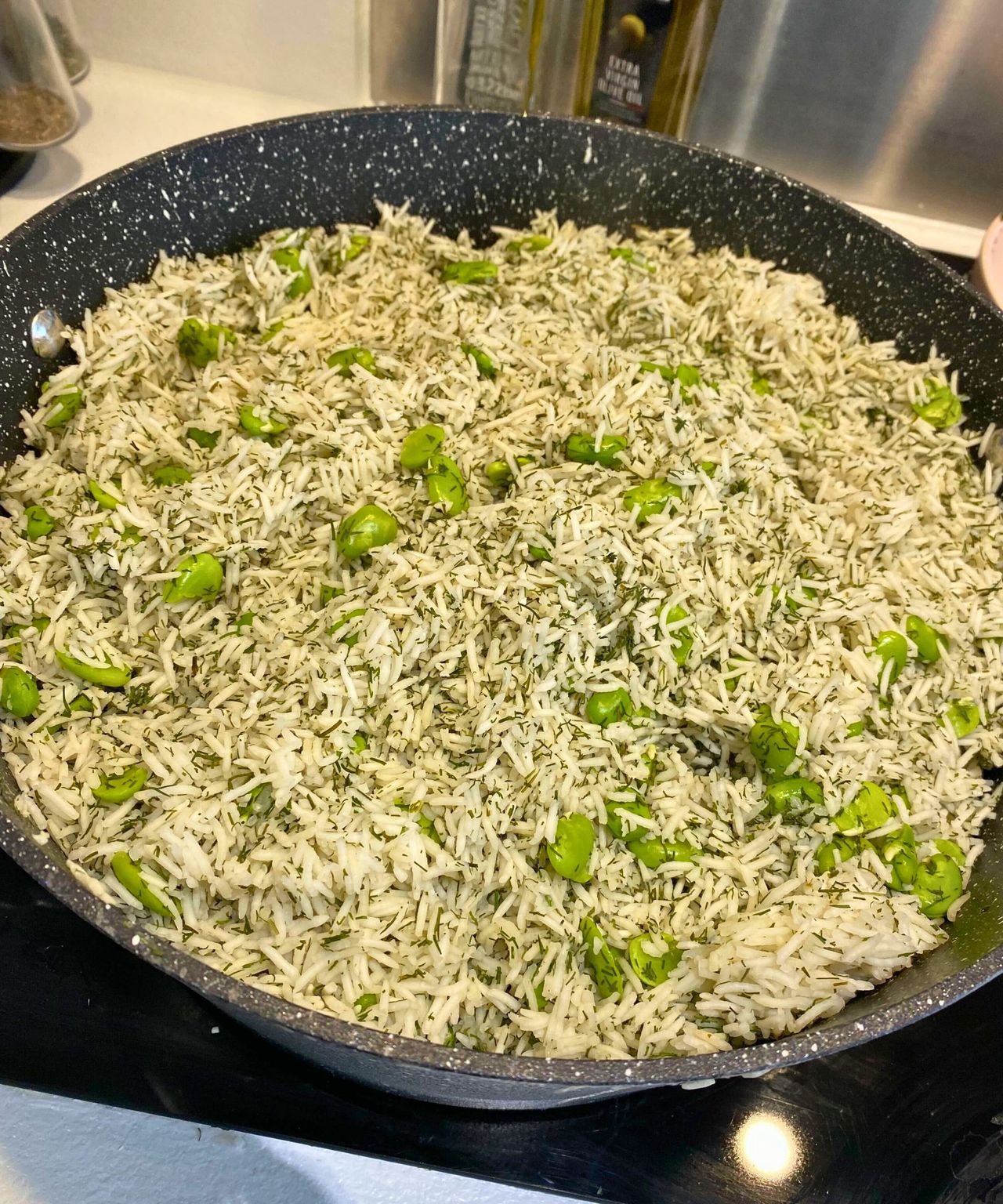 My Persian dill and broad bean rice. It it largely green, and seen filling to the top of a black deep pot on a glass stovetop