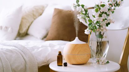 An electric diffuser in bedroom with essential oils in brown glass bottle with vase and floral stems