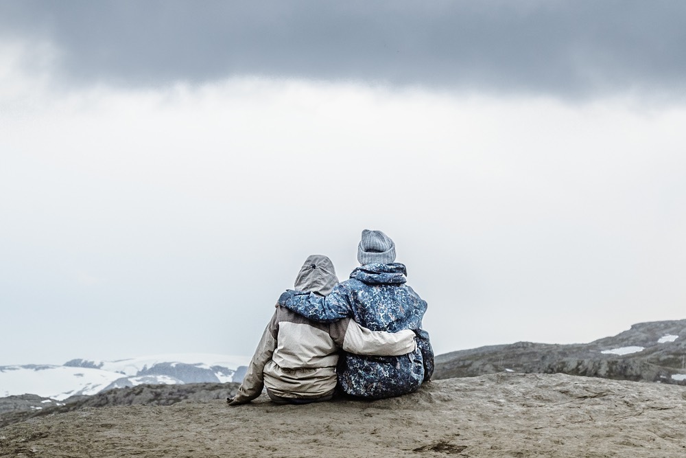 Young happy couple in love, sitting at the edge of cliff looking away.