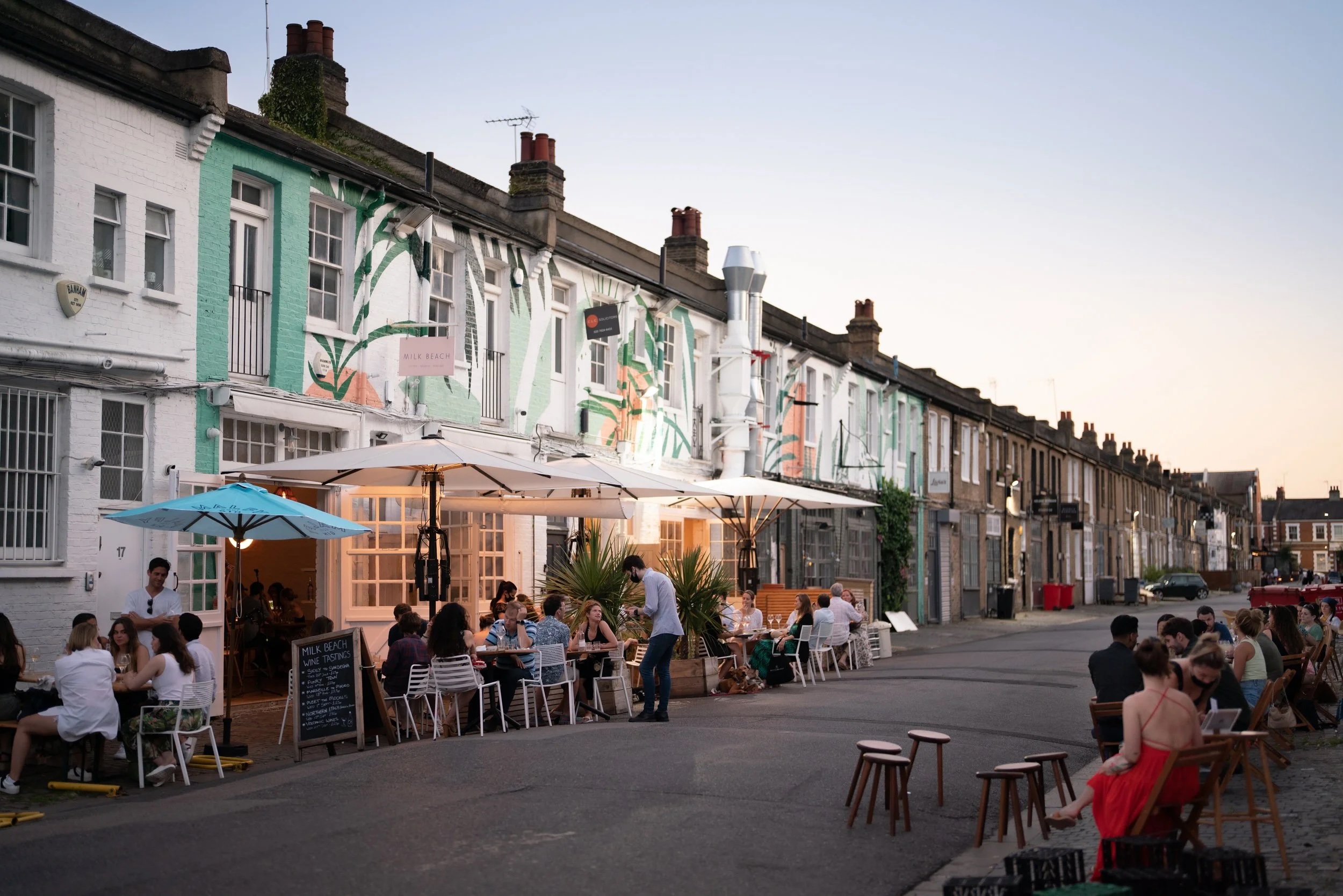 A row of terraced buildings with tables and parasols on the street infront