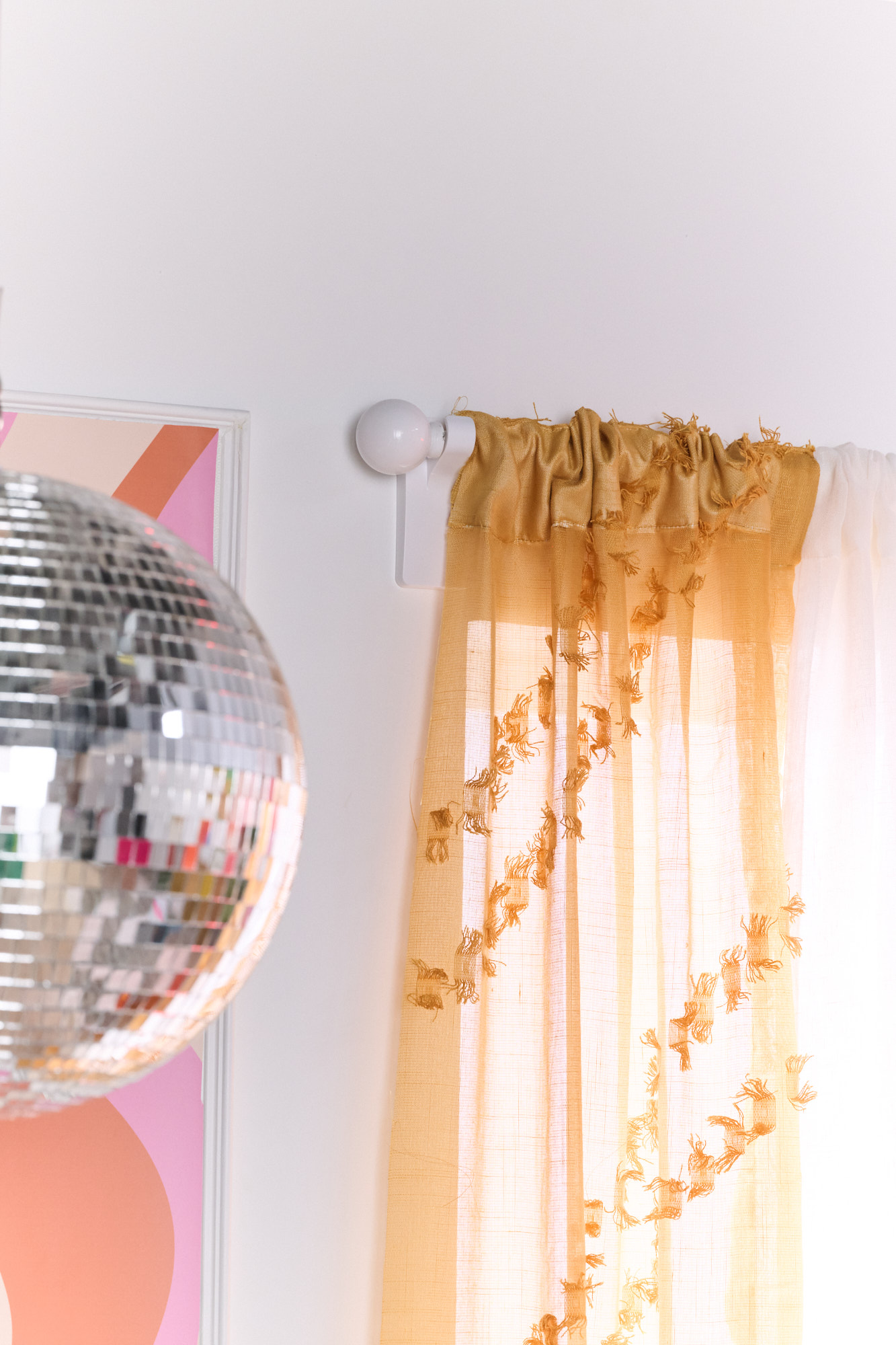 Dorm room window outfitted with sheer mustard yellow curtains and a disco ball