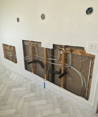 A modern bathroom with beige wall paint decor, Herringbone flooring decor and space prepared for quartz countertop and sanitaryware plumbing