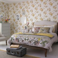 bedroom with floral wall wooden bed with floral cushion and white wooden flooring