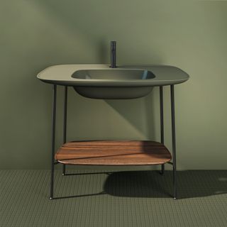 Olive green textured floor, olive green wall, olive green wash basin set on four metal legs, dark wood grain bottom shelf, black tap