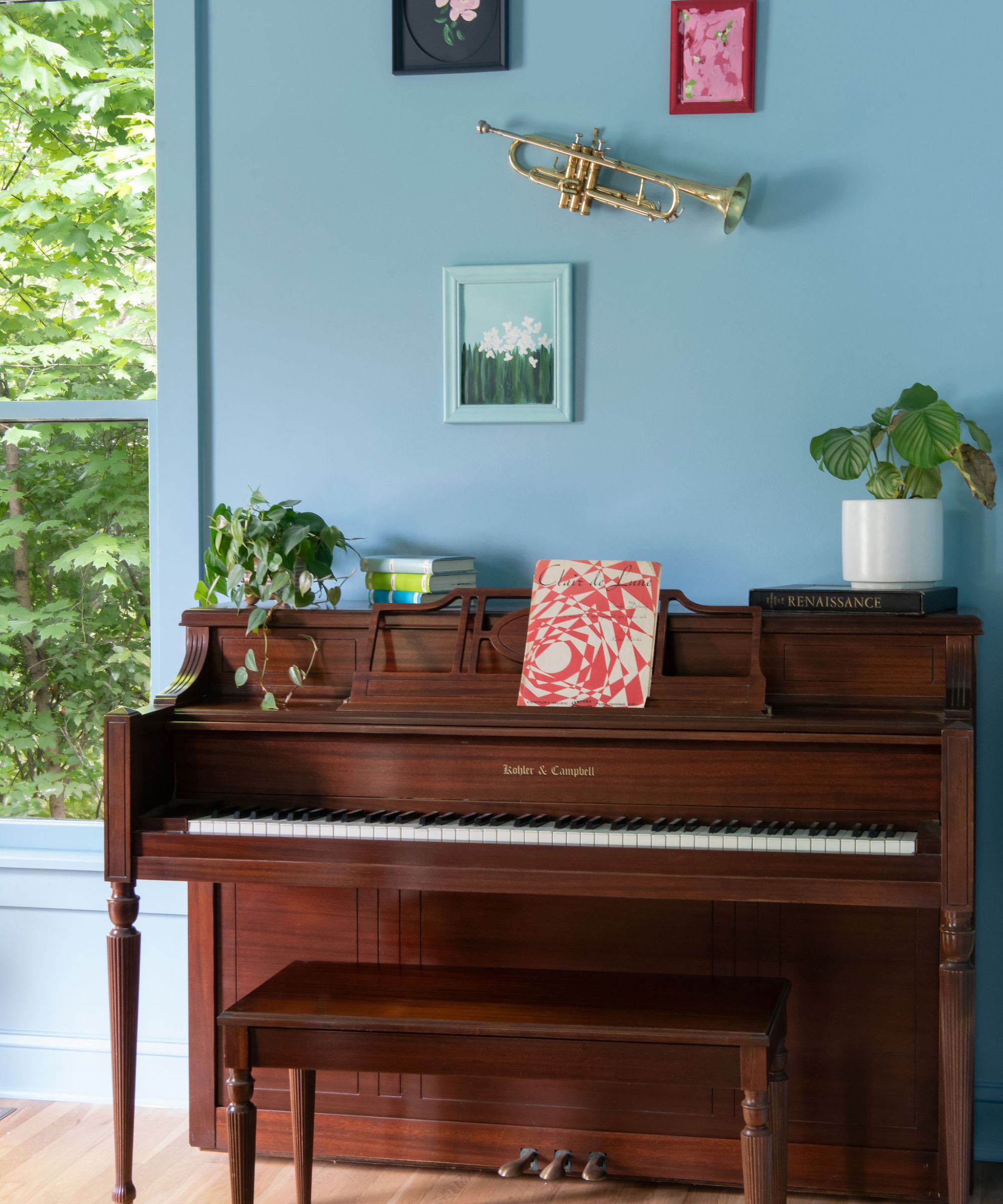 A blue color-drenched room with a wooden piano and a gallery wall above it.