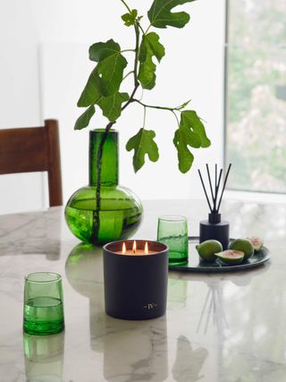 scented candle on marble table with green glass vase