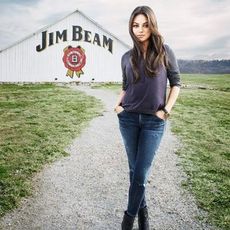 Mila Kunis posing on gravel path, in front of Jim Bean barn