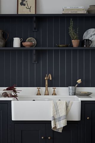 charcoal kitchen with white sink and countertop, white walls above, wooden floor, brass antique tap, stool, open shelving