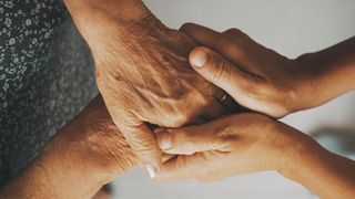 A closeup of a younger woman holding the hands of an elderly woman