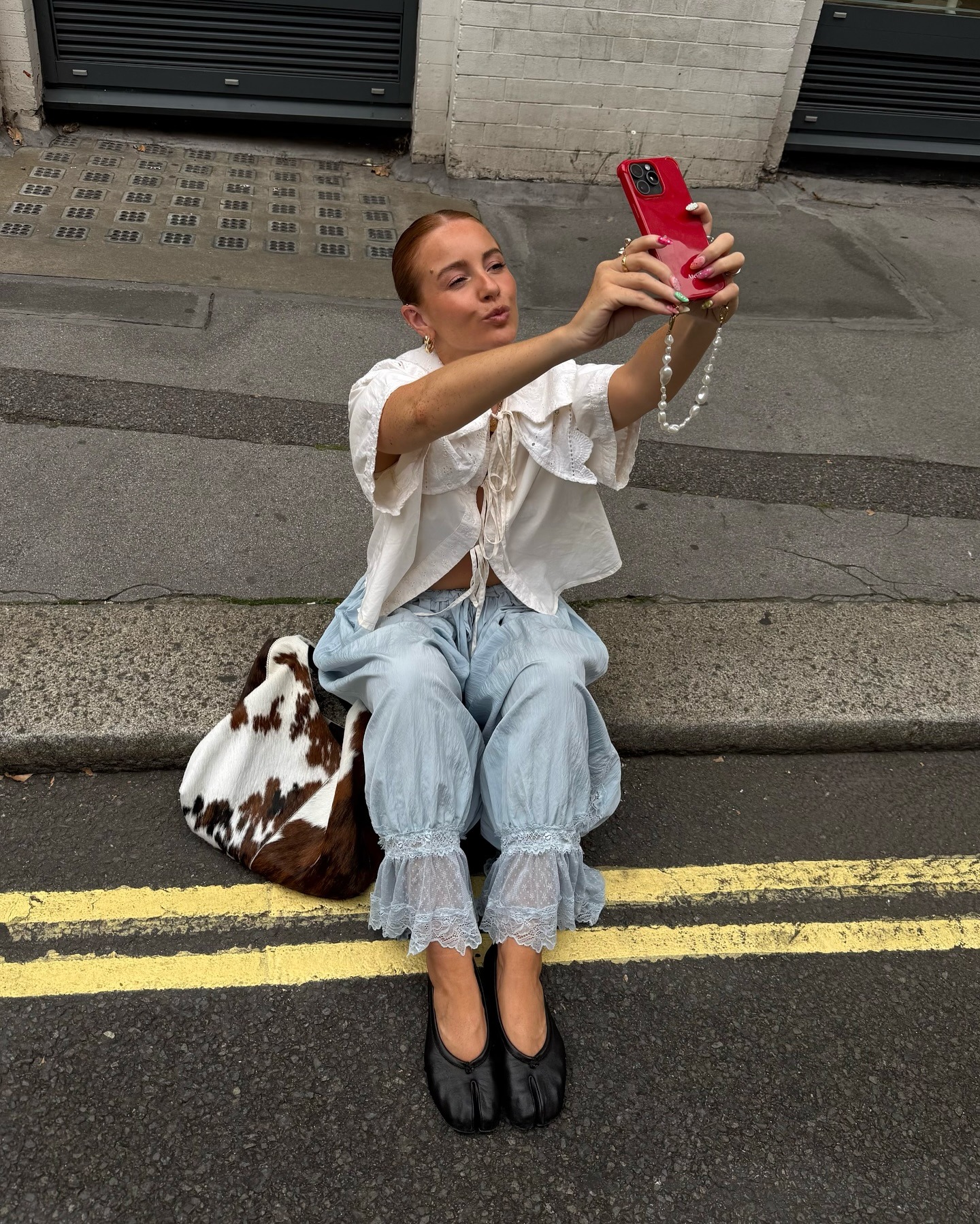 Fashion person Rebecca Wyatt wears a boho outfit idea. She wears a bloomer trouser, blouse and tabi shoes in a recent image from her Instagram, her cowprint bag is on the ground next to her as she takes a selfie.