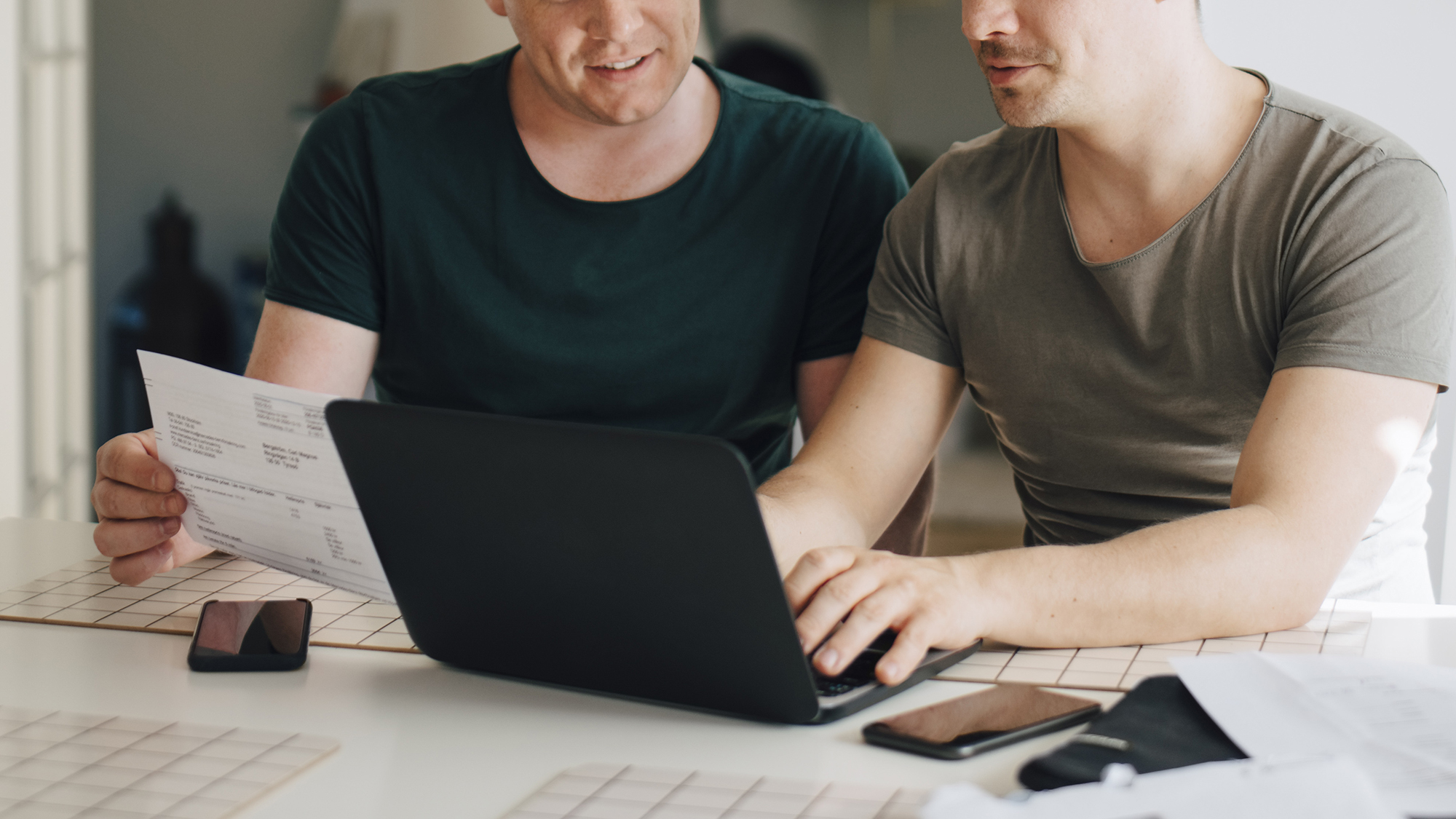 Gay couple at home looking at documents and laptop computer