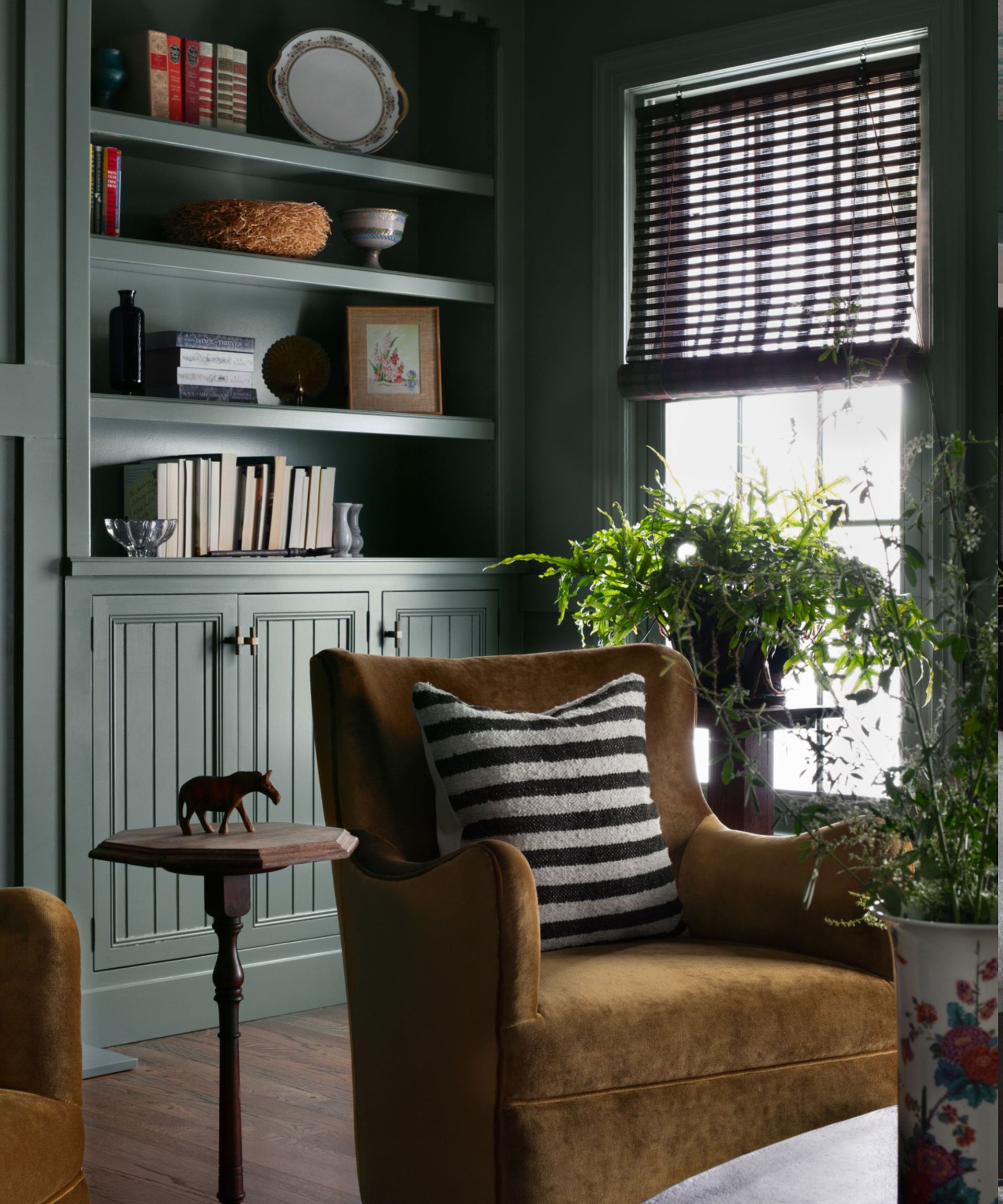 A green home library with a window and a gold velvet chair