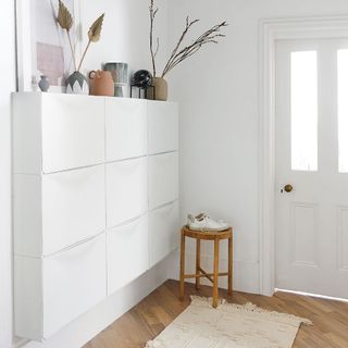 White hallway with wall-mounted storage and vases with décor and a floor rug