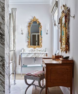 A marble bathroom with wall lighting and gold mirrors