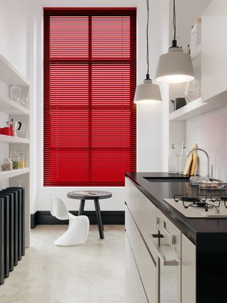 a small, slim, white kitchen with contemporary scheme, with red window blinds, modern chair and a bar stool by english blinds