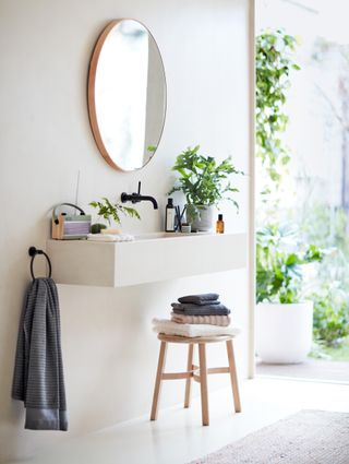 A wall hung vanity unit with a mirror over and a stool beneath