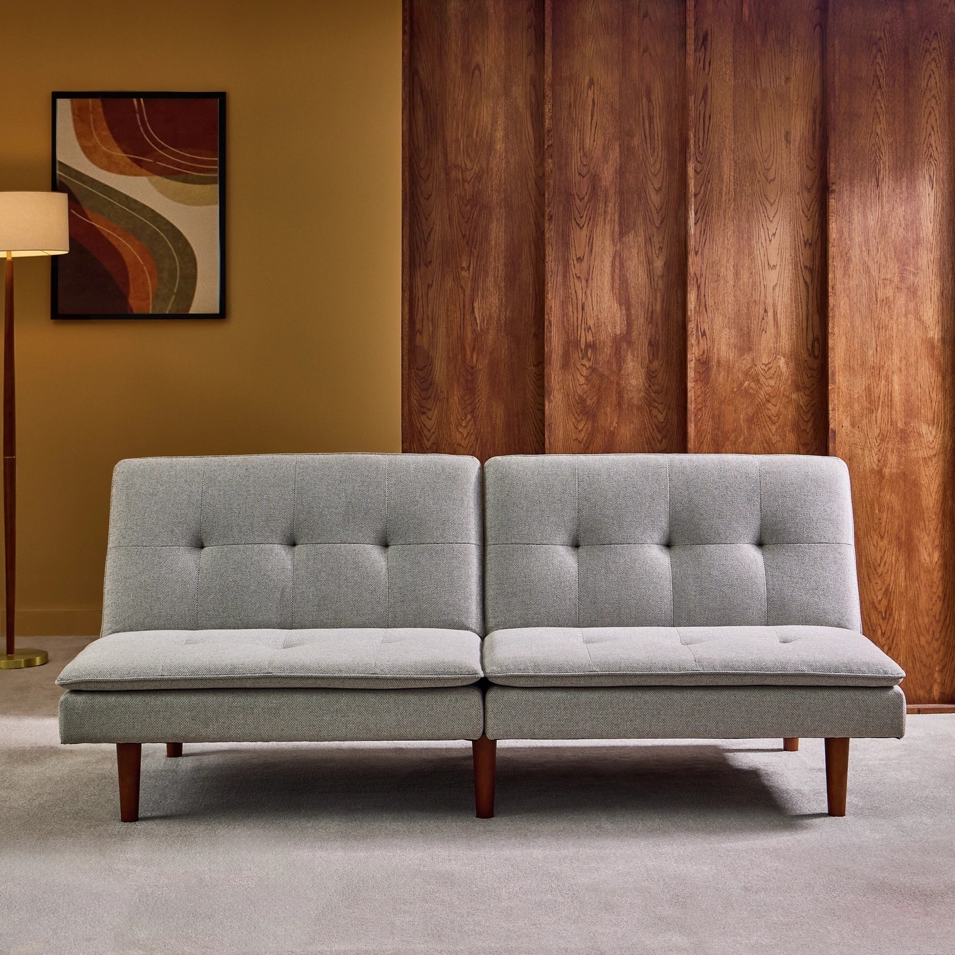 A gray, mid-century modern style sofa in a room with light gray carpeting and walls that are half wood panelling, half yellow paint.