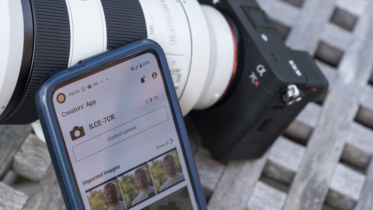 Mobile phone with Sony Creators' App on screen and Sony A7C R mirrorless camera outside on a wooden table in the background