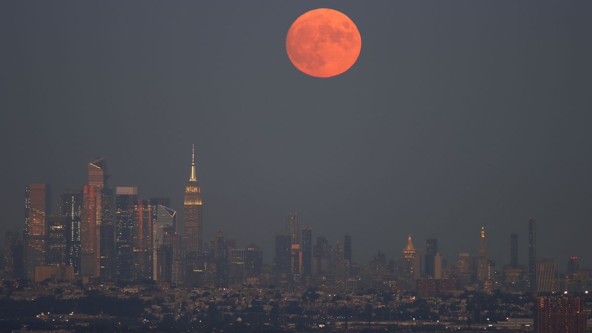 The Harvest Moon rises behind the skyline of midtown Manhattan and the Empire State Building as the sun sets in New York City on September 9, 2022, as seen from West Orange, New Jersey.