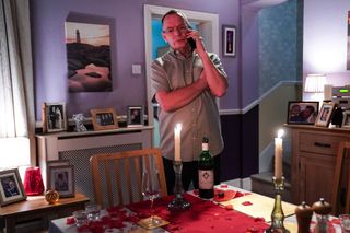 Ian Beale on his mobile standing next to a table laid with a candlelit meal in the Beale house